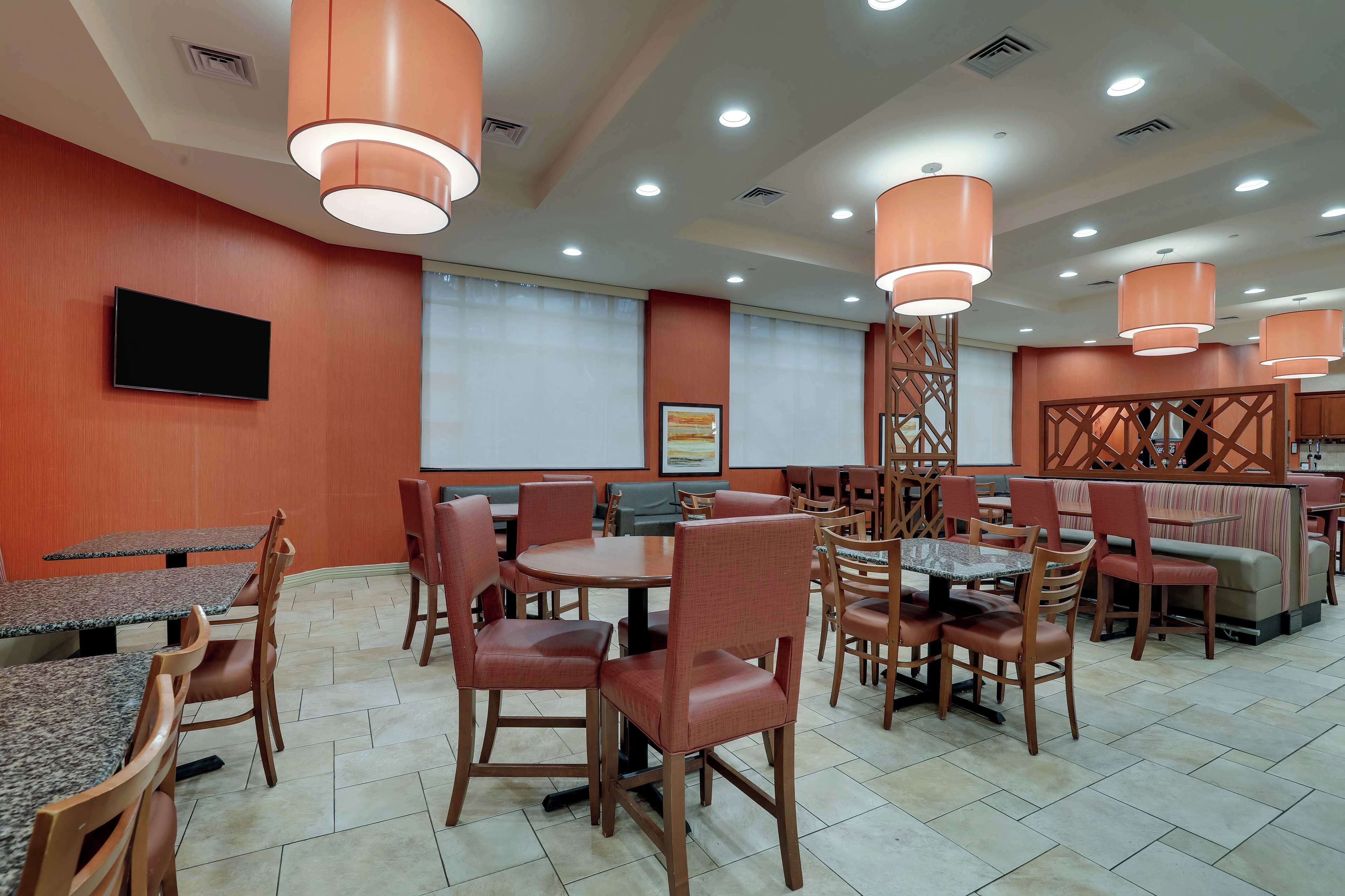 A restaurant with multiple tables and chairs, a flat-screen TV mounted on the wall, and pendant lighting.