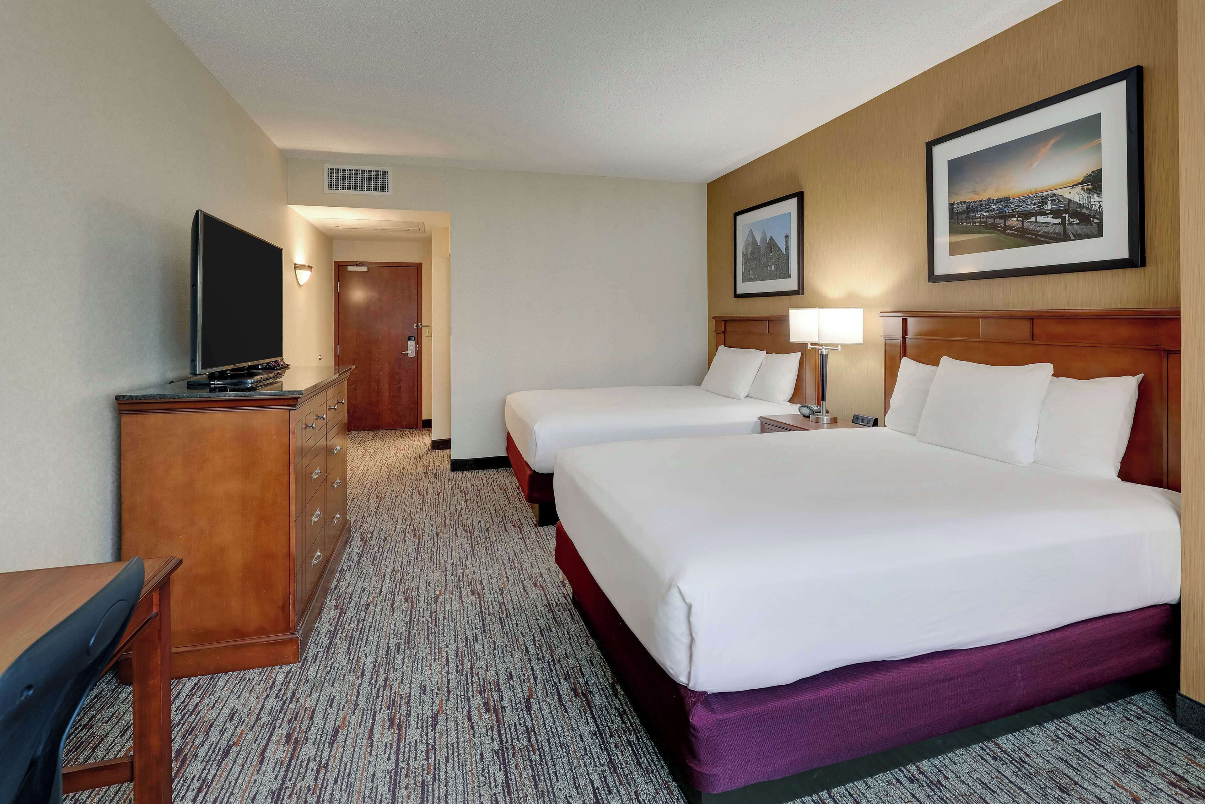 A hotel room with two beds, a desk, a TV, and a dresser.