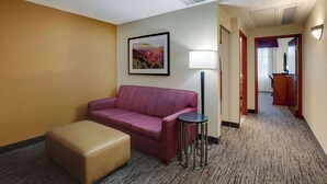 A hotel room with a sofa, ottoman, lamp, and a framed picture on the wall. - Drury Inn & Suites Charlotte Northlake (Charlotte)