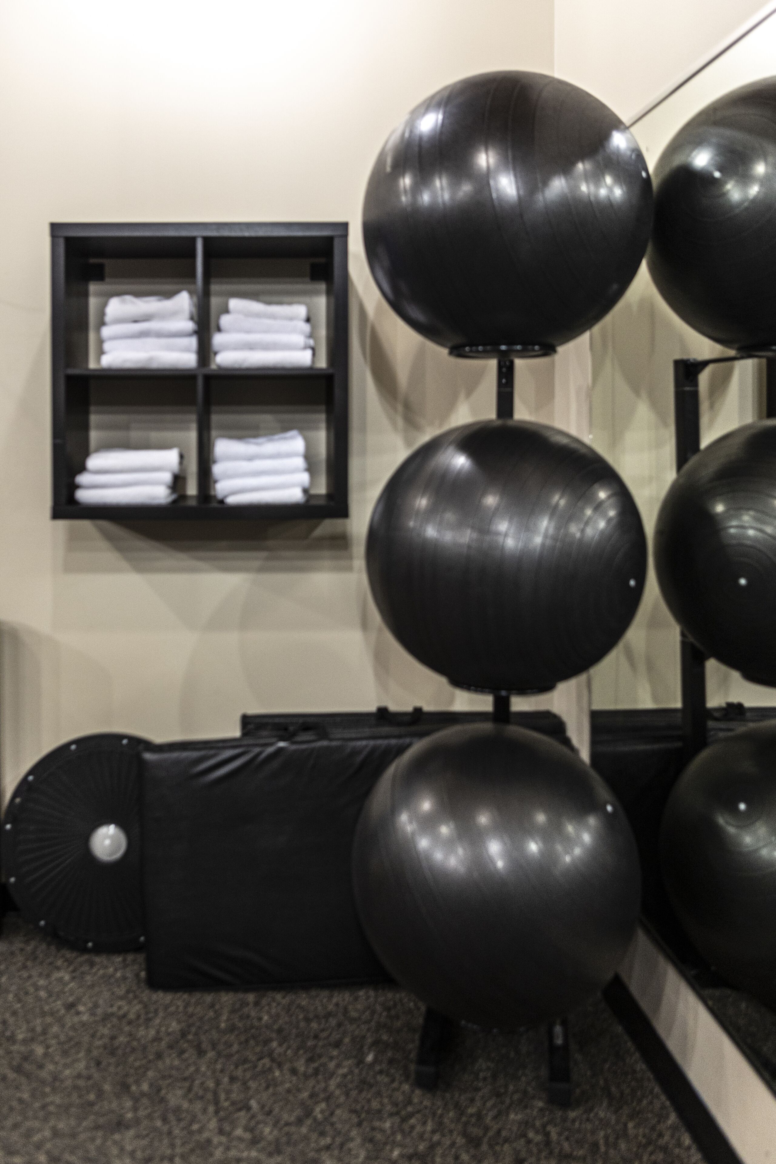 A gym with exercise balls, a black shelf with folded towels, and a black massage table.