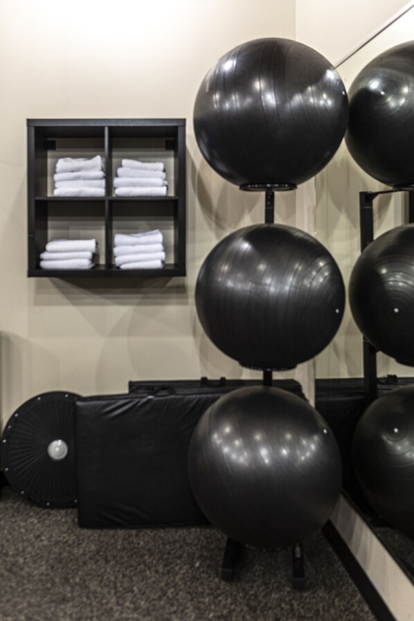 Un gimnasio con pelotas de ejercicio, un estante negro con toallas dobladas y una mesa de masaje negra.