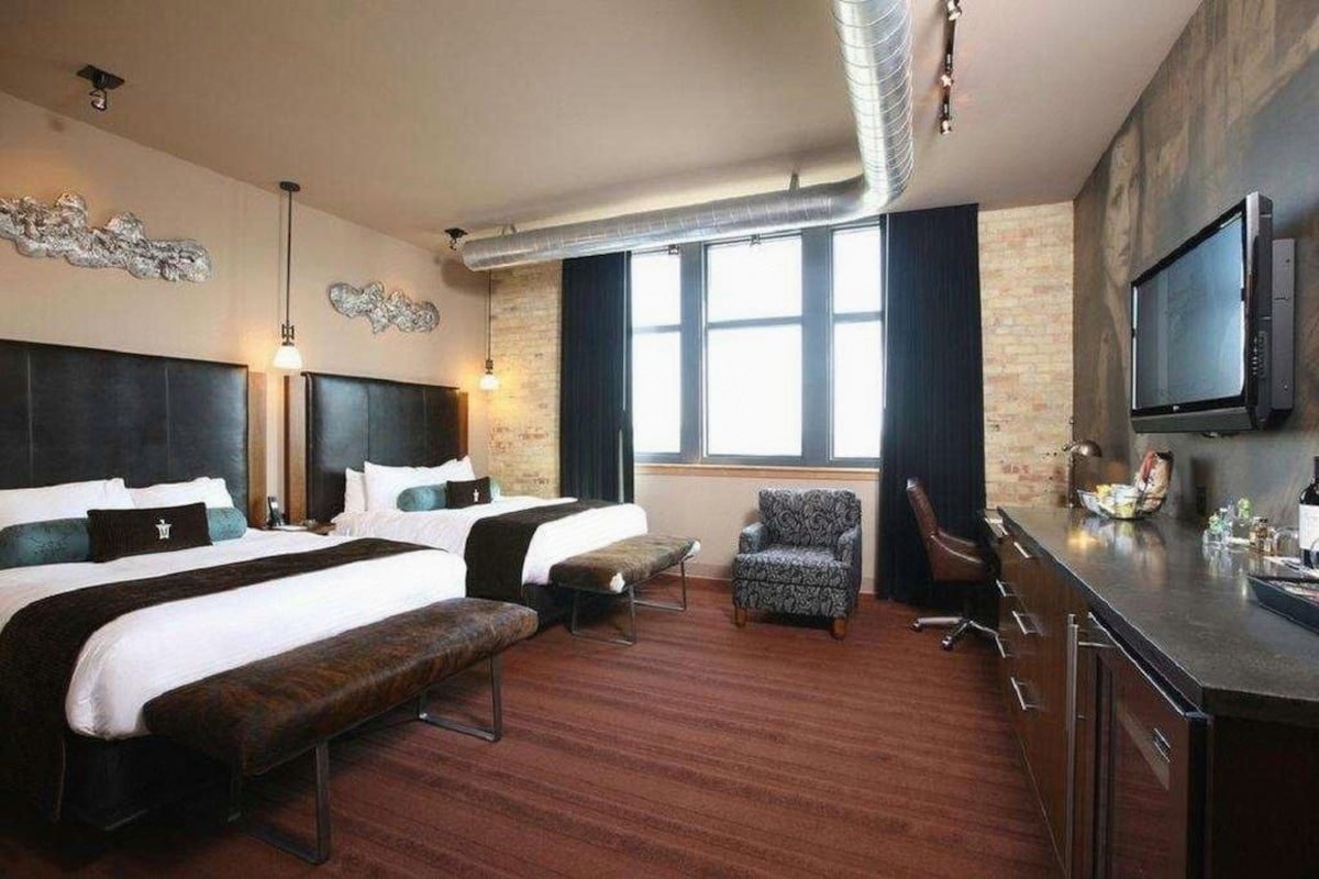 A hotel room with two beds, a desk, a chair, and a TV.