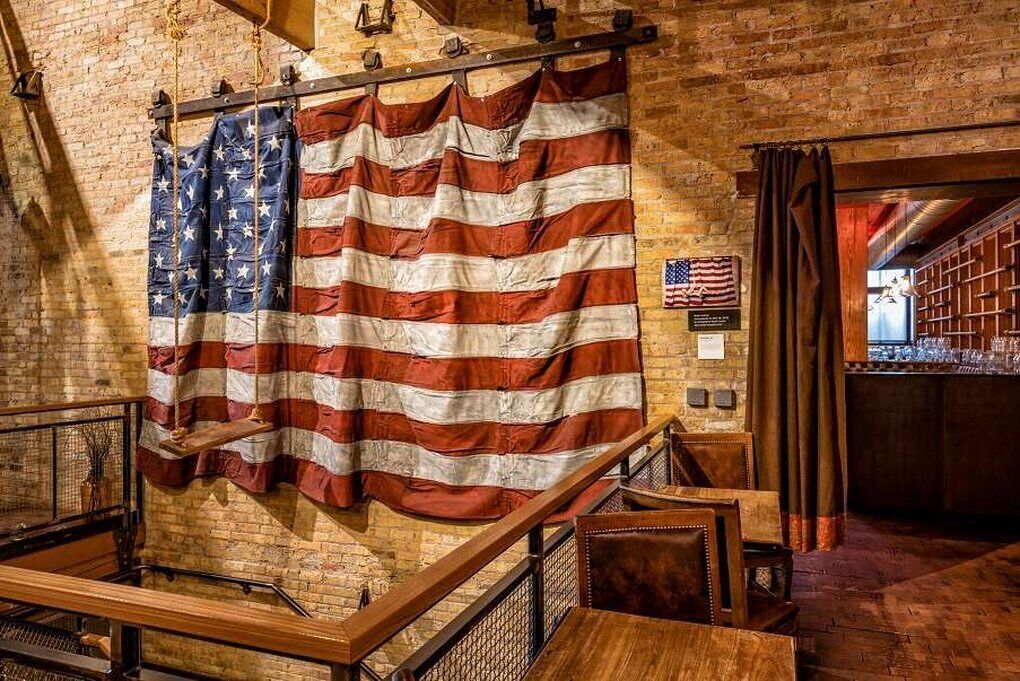 Een bakstenen muur met een Amerikaanse vlag en een kleinere vlag, een trap en een barruimte met kasten.