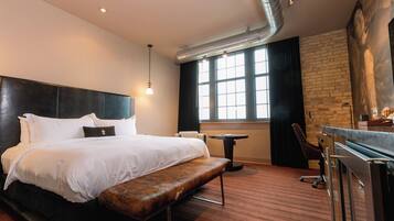 A hotel room with a large bed, a bench, a small table, a desk, and a large window.