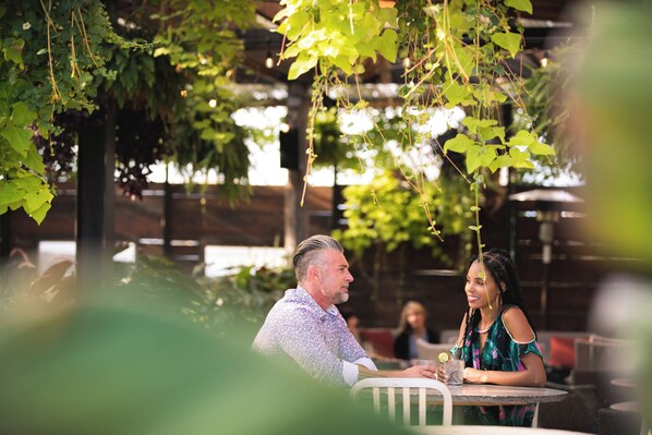 An outdoor dining area with tables and chairs, surrounded by greenery and a wooden fence. - The Iron Horse Hotel (Milwaukee)
