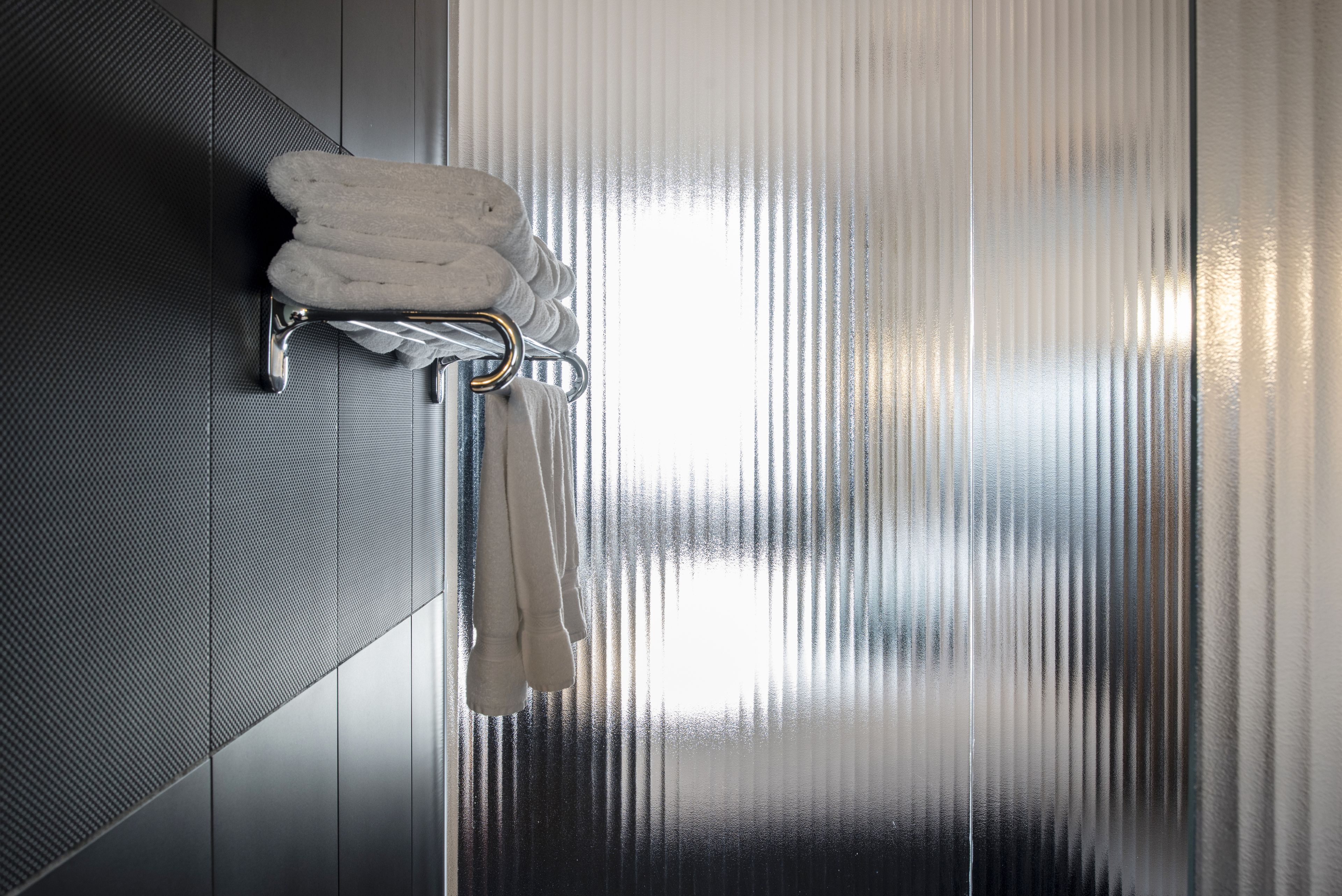 A bathroom with a towel rack holding three towels and a hand dryer.