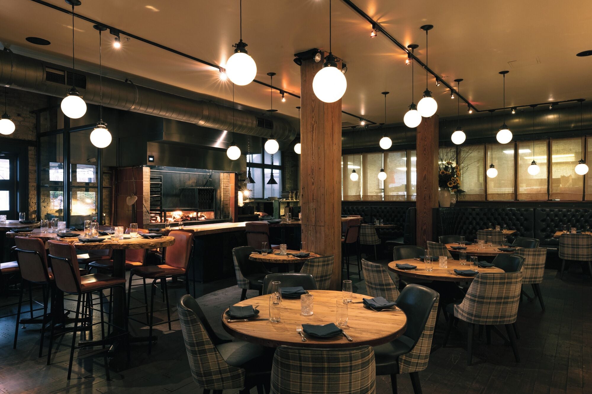 A restaurant interior with round tables, plaid chairs, and hanging spherical lights.