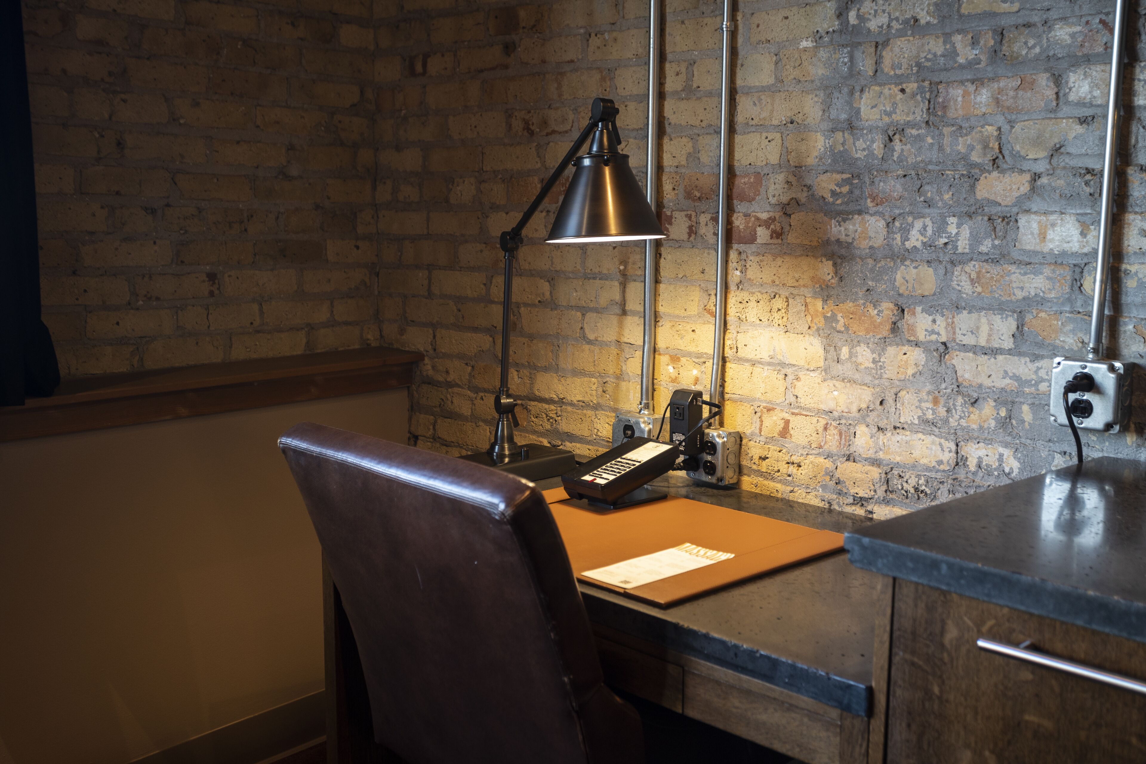 A workspace with a desk, chair, lamp, and brick wall.