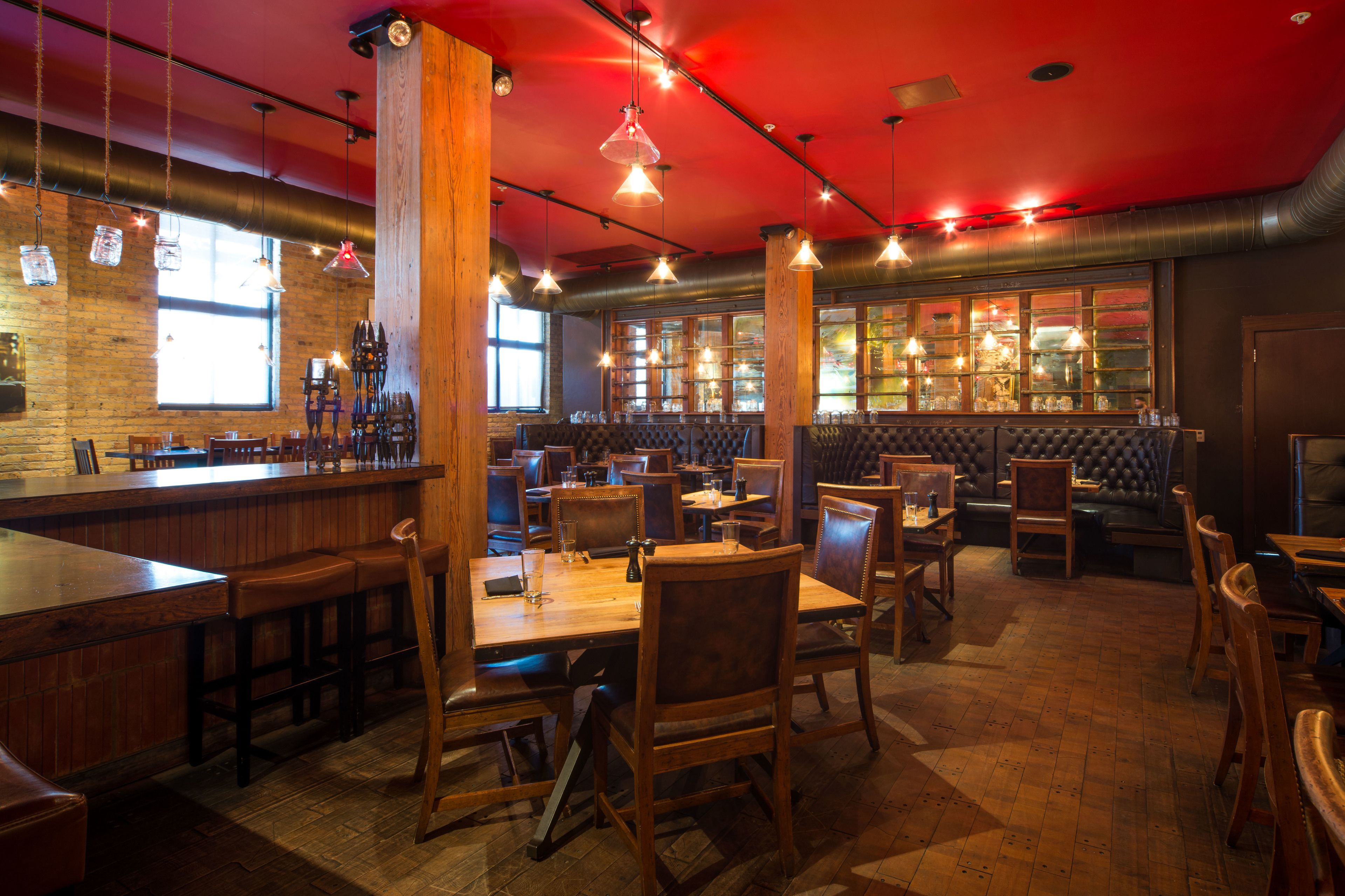 A restaurant with wooden tables and chairs, a bar area, and large windows.
