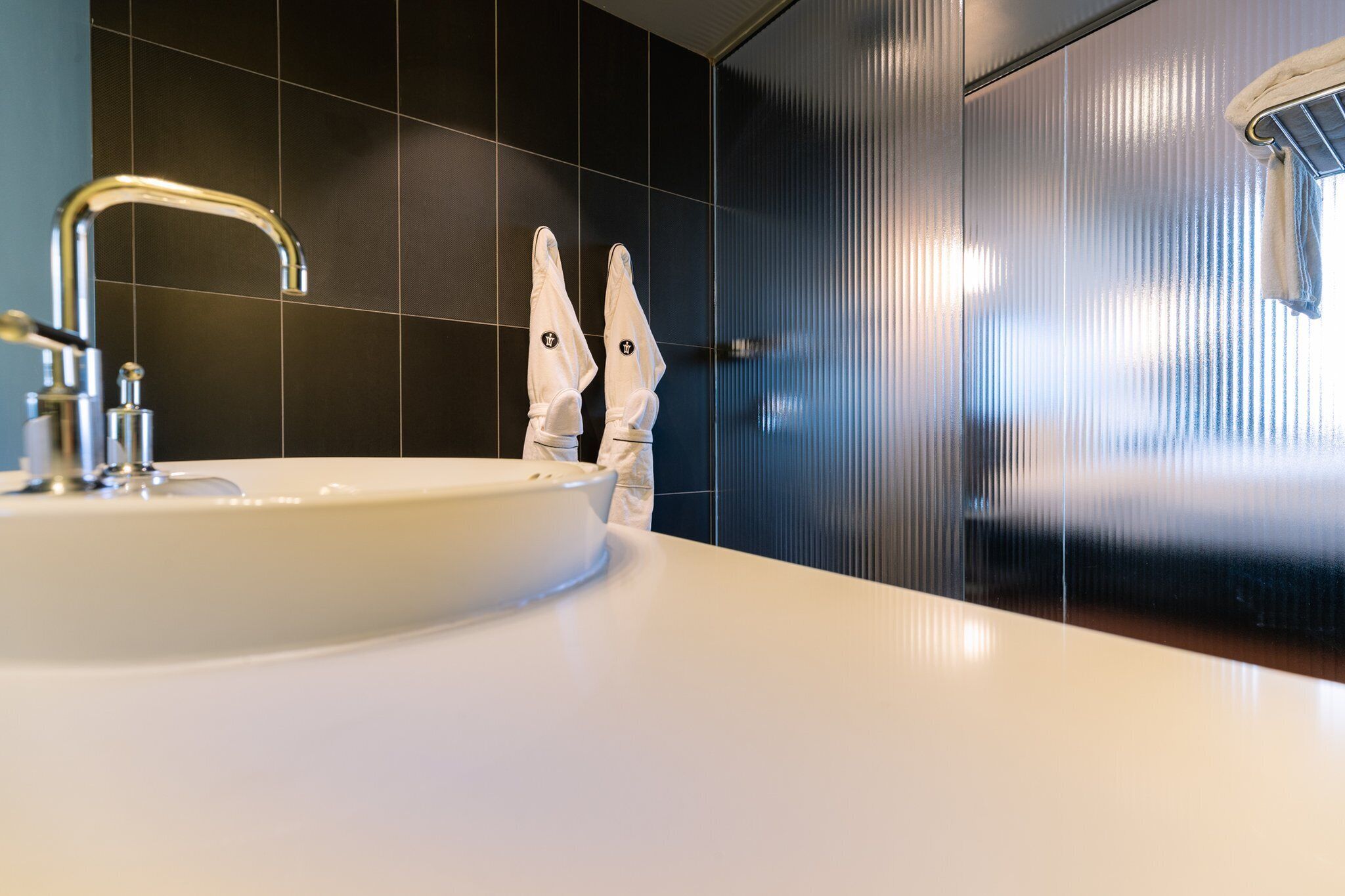 Un baño moderno con un lavamanos blanco, grifo cromado y perchero.