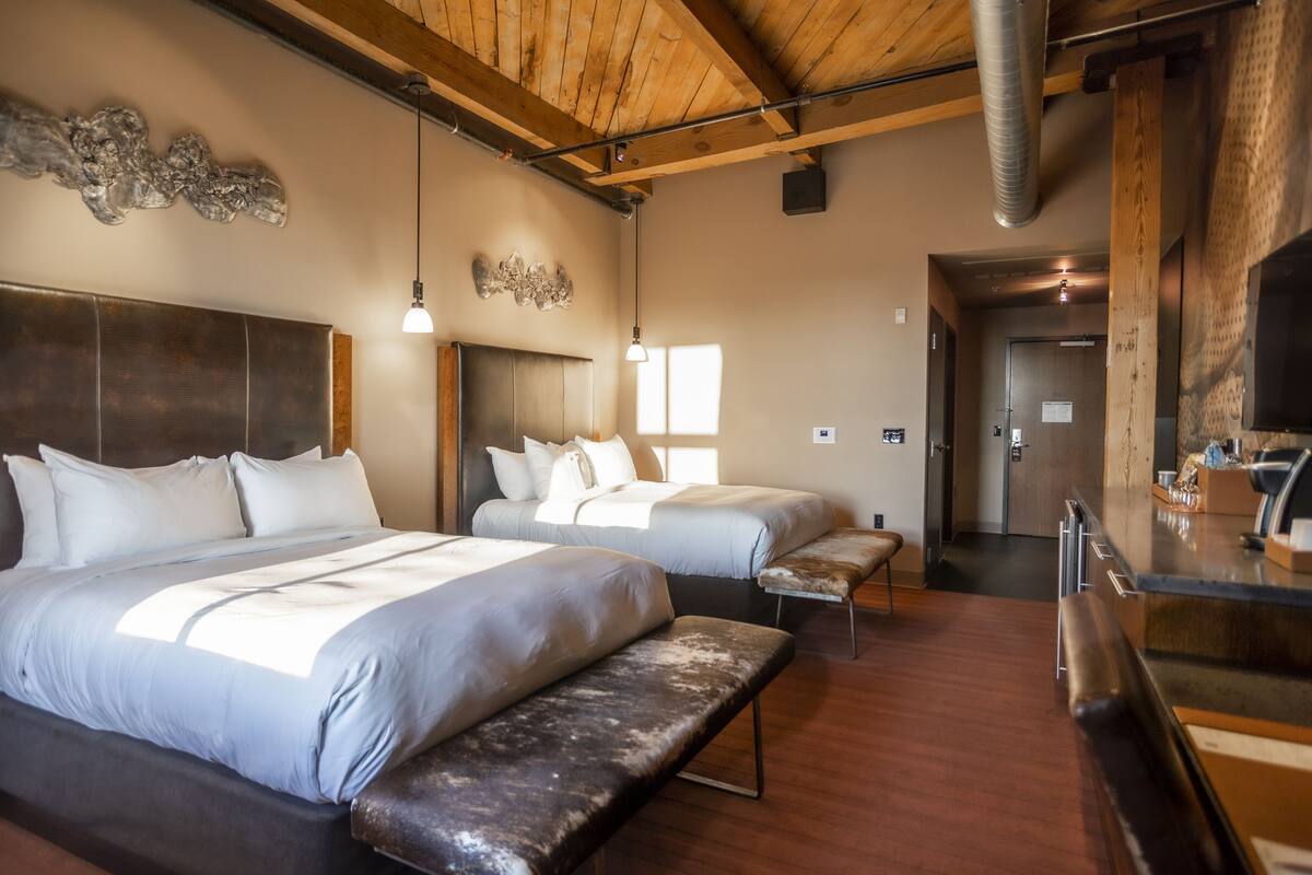 Ein Hotelzimmer mit zwei Betten, einer Bank, einem Schreibtisch und einem großen Spiegel.