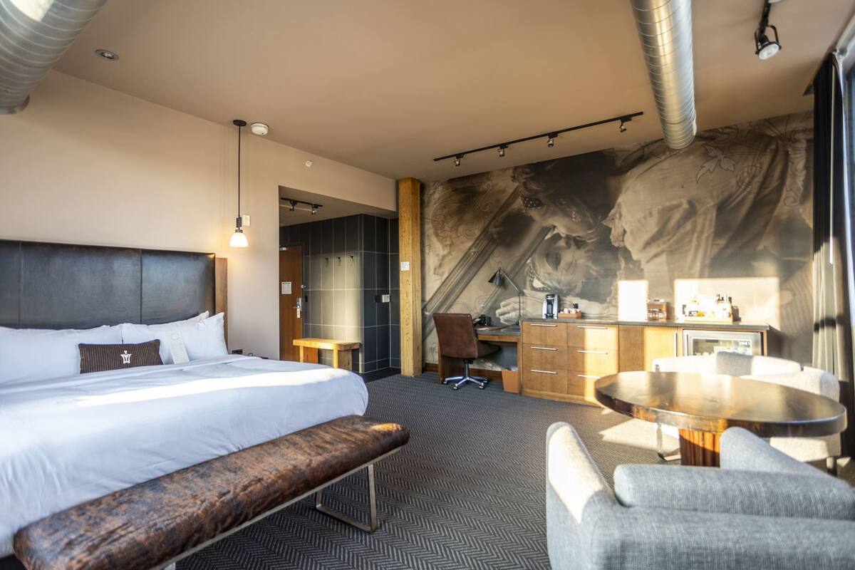 Ein Hotelzimmer mit Bett, Schreibtisch, Stuhl, Bank und kleinem Tisch.
