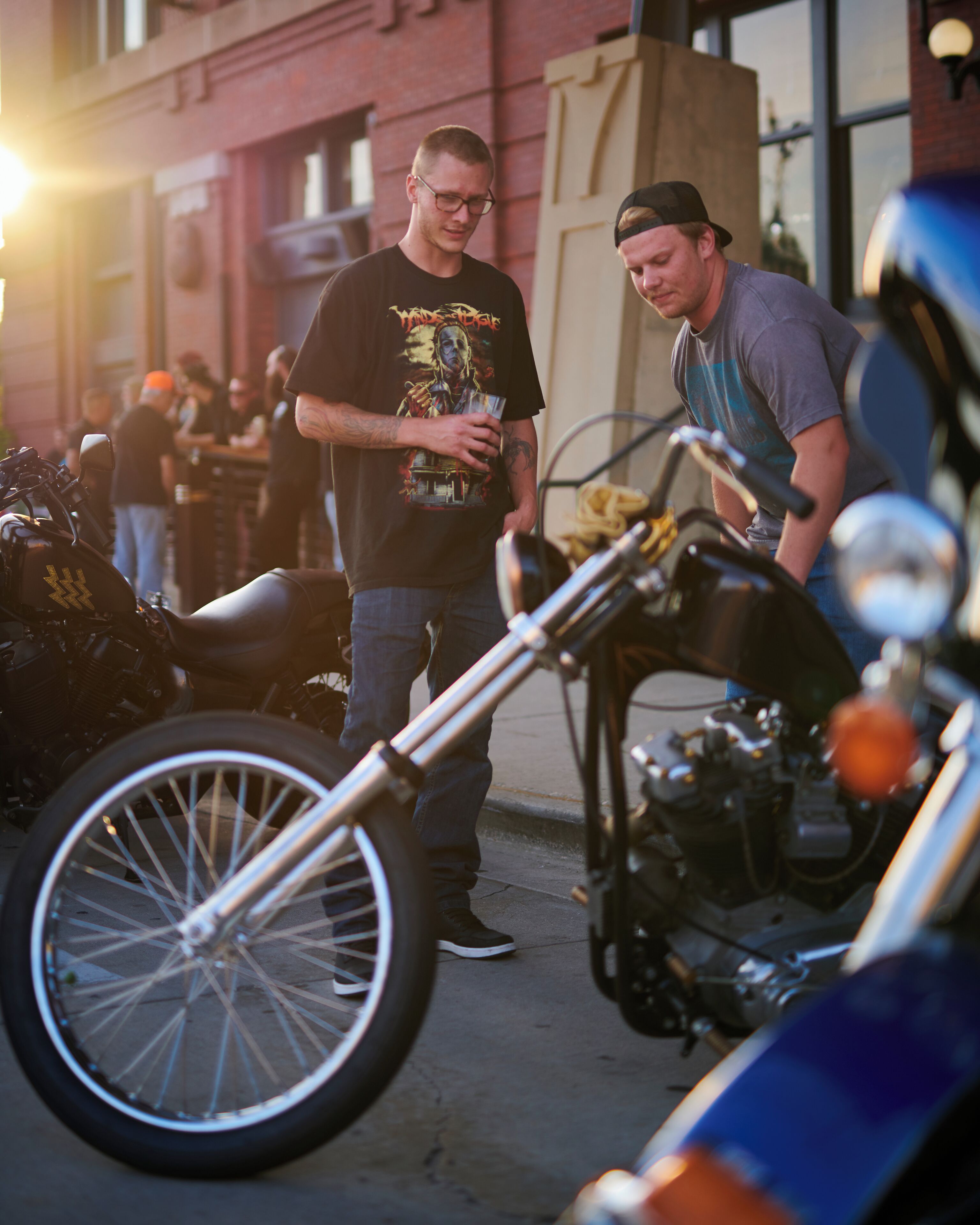 Dos hombres cerca de motocicletas, uno sosteniendo una bebida.