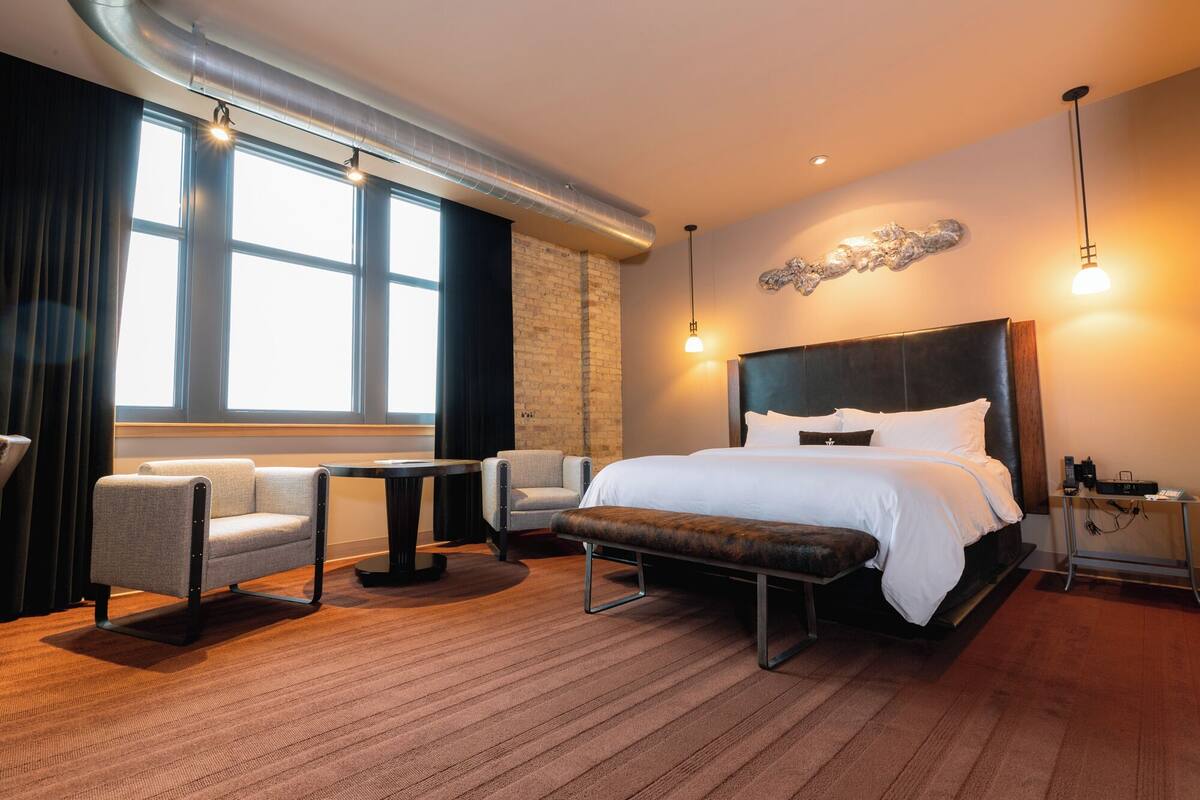Ein modernes Hotelzimmer mit einem großen Bett, zwei Sesseln, einem kleinen Tisch und einer Bank.