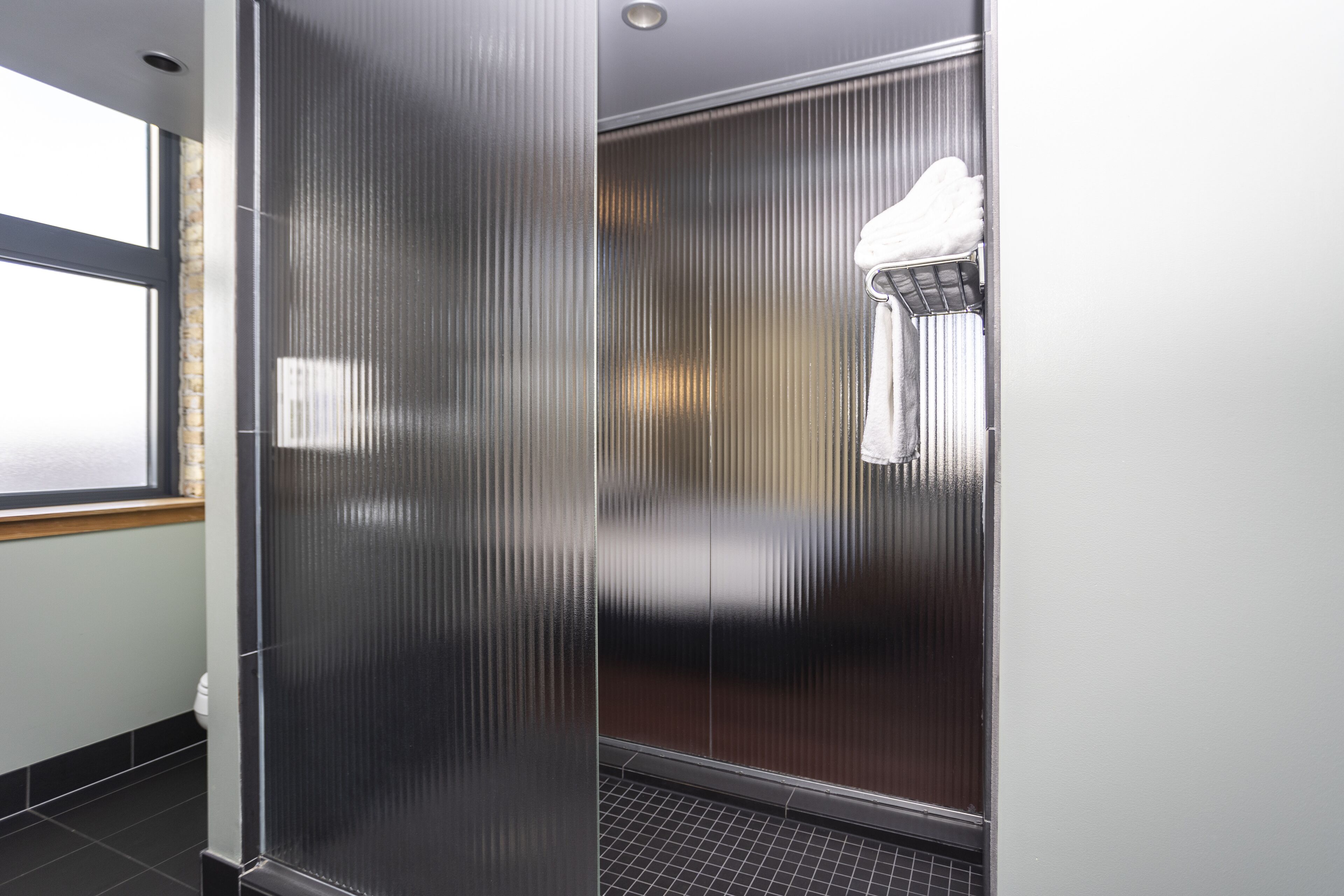 A modern bathroom with a glass partition, a towel rack, and a window.