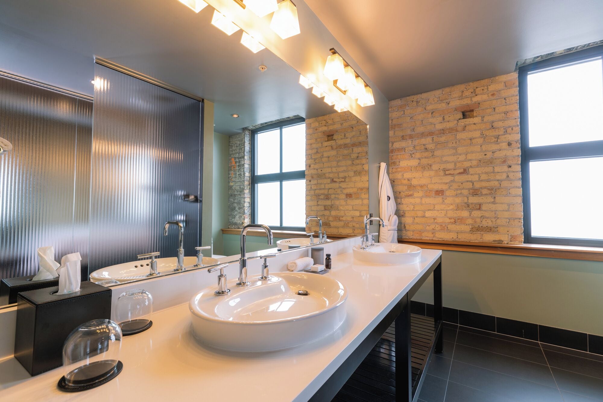 Un baño moderno con dos lavamanos, un espejo grande y una pared de ladrillo.