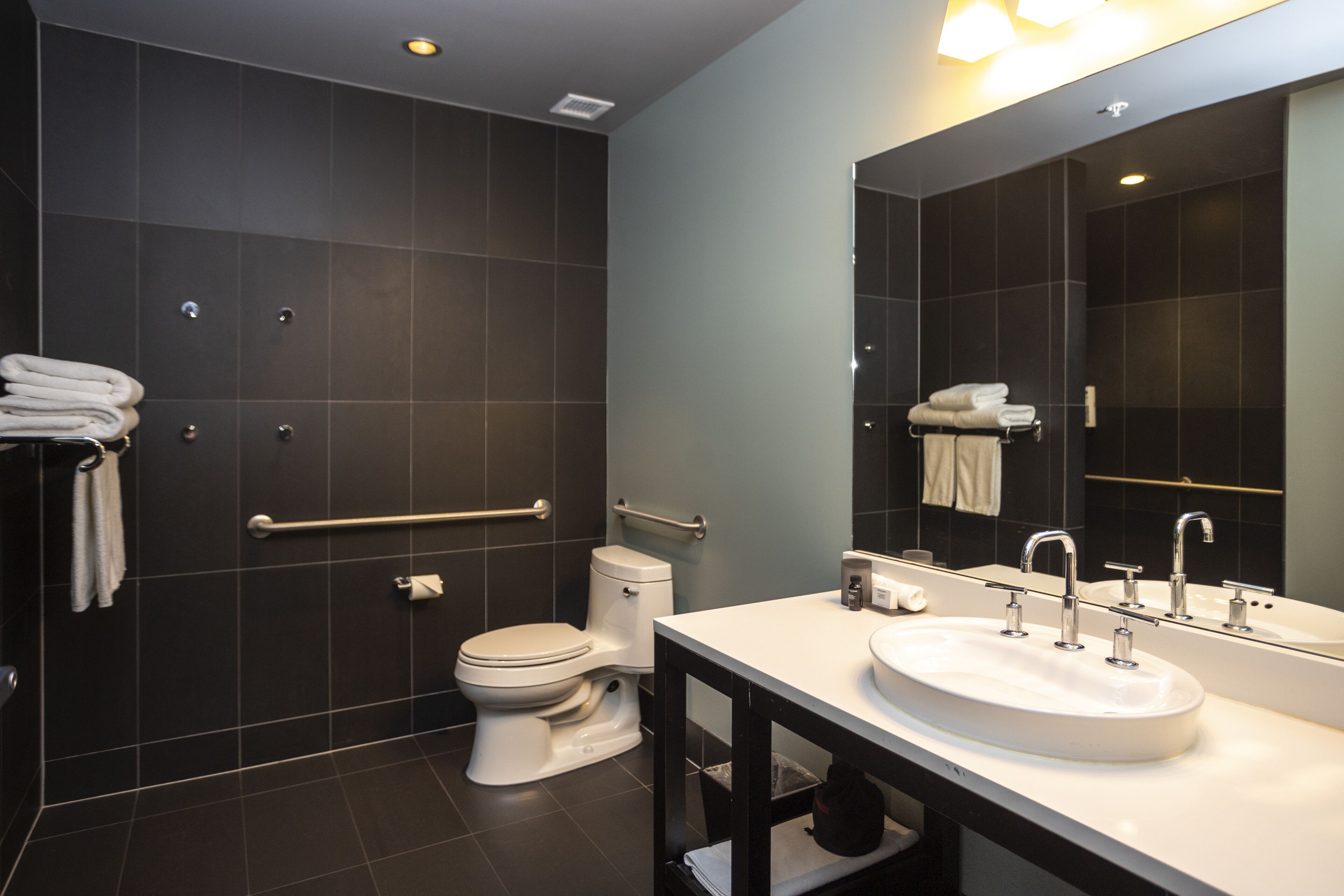 Un baño moderno con un lavabo blanco, dos espejos, un inodoro y una zona de ducha.