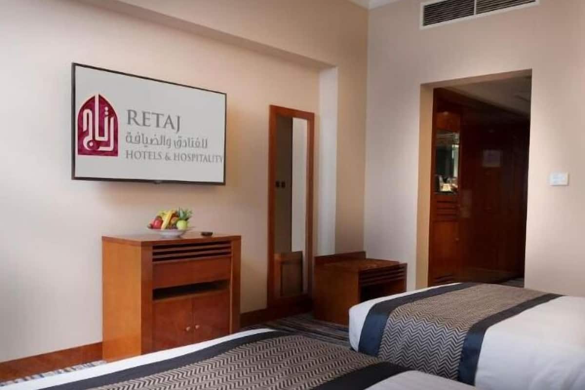 A hotel room with two beds, a wooden cabinet, and a sign for RETAJ Hotels & Hospitality.