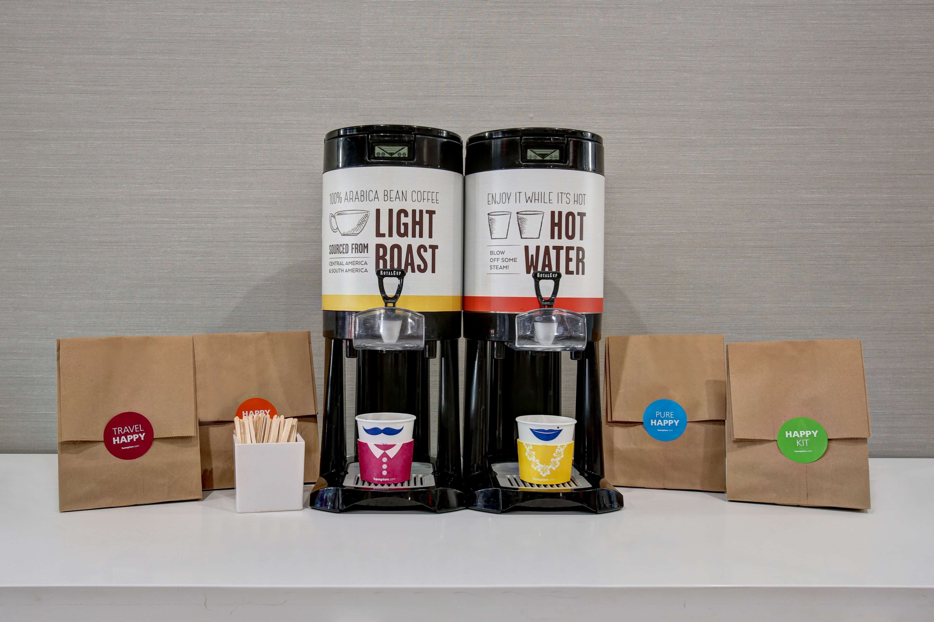 Two coffee machines labeled "Light Roast" and "Hot Water" with coffee cups and travel-themed bags.