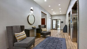 A hotel lobby with grey upholstered chairs, a round mirror, a wooden floor, and a welcome mat. - Hampton Inn & Suites Dallas-DeSoto (DeSoto)