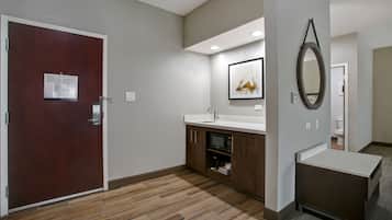 A hotel bathroom with a wooden floor, a sink, a mirror, and a door with a notice.