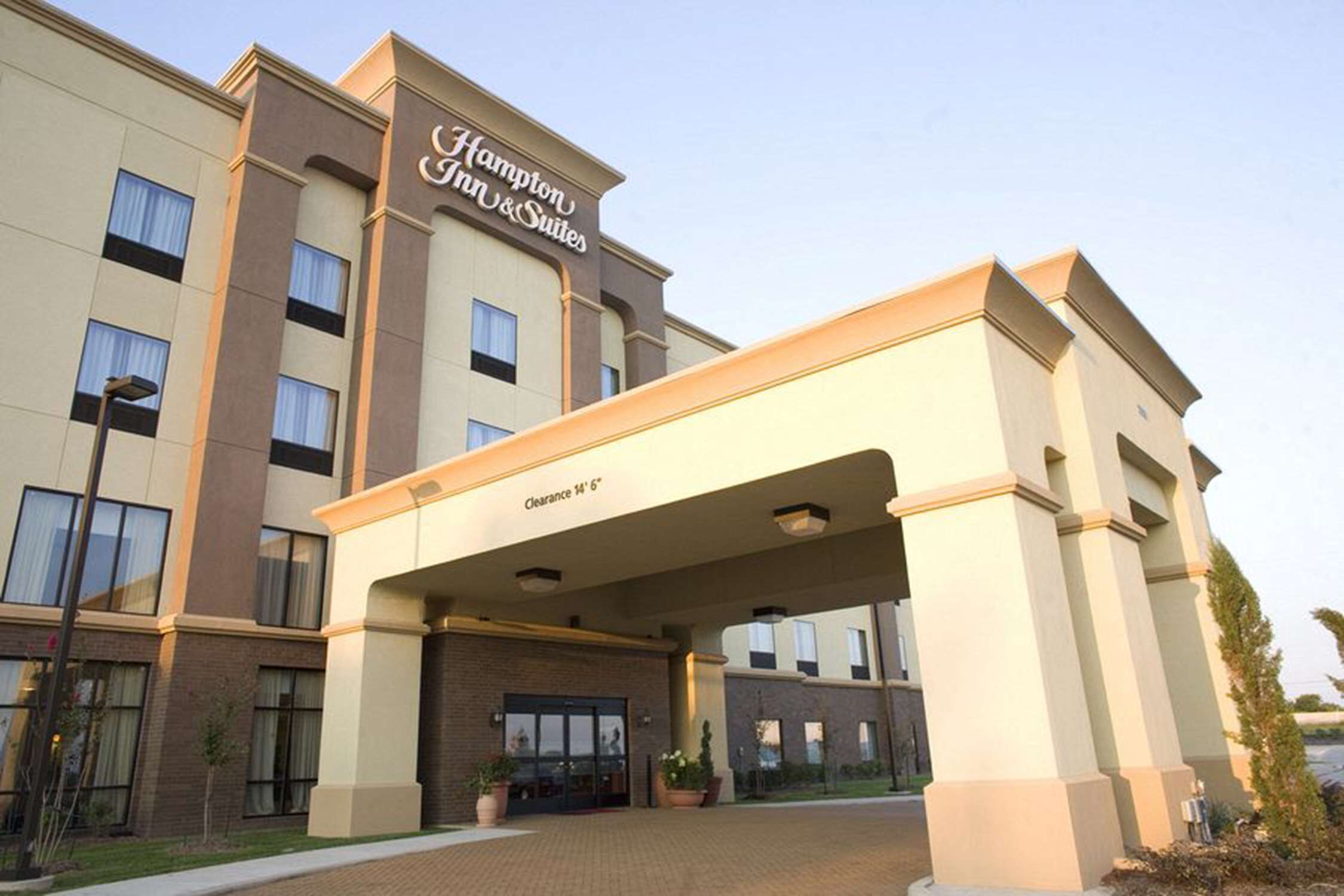 A Hampton Inn & Suites hotel entrance with a clear sign, a covered walkway, and a brick pathway.