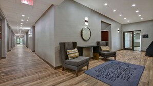 A hotel lobby with a long corridor, seating area with chairs and a small table, a mirror on the wall, and a welcome mat on the floor. - Hampton Inn & Suites Dallas-DeSoto (DeSoto)