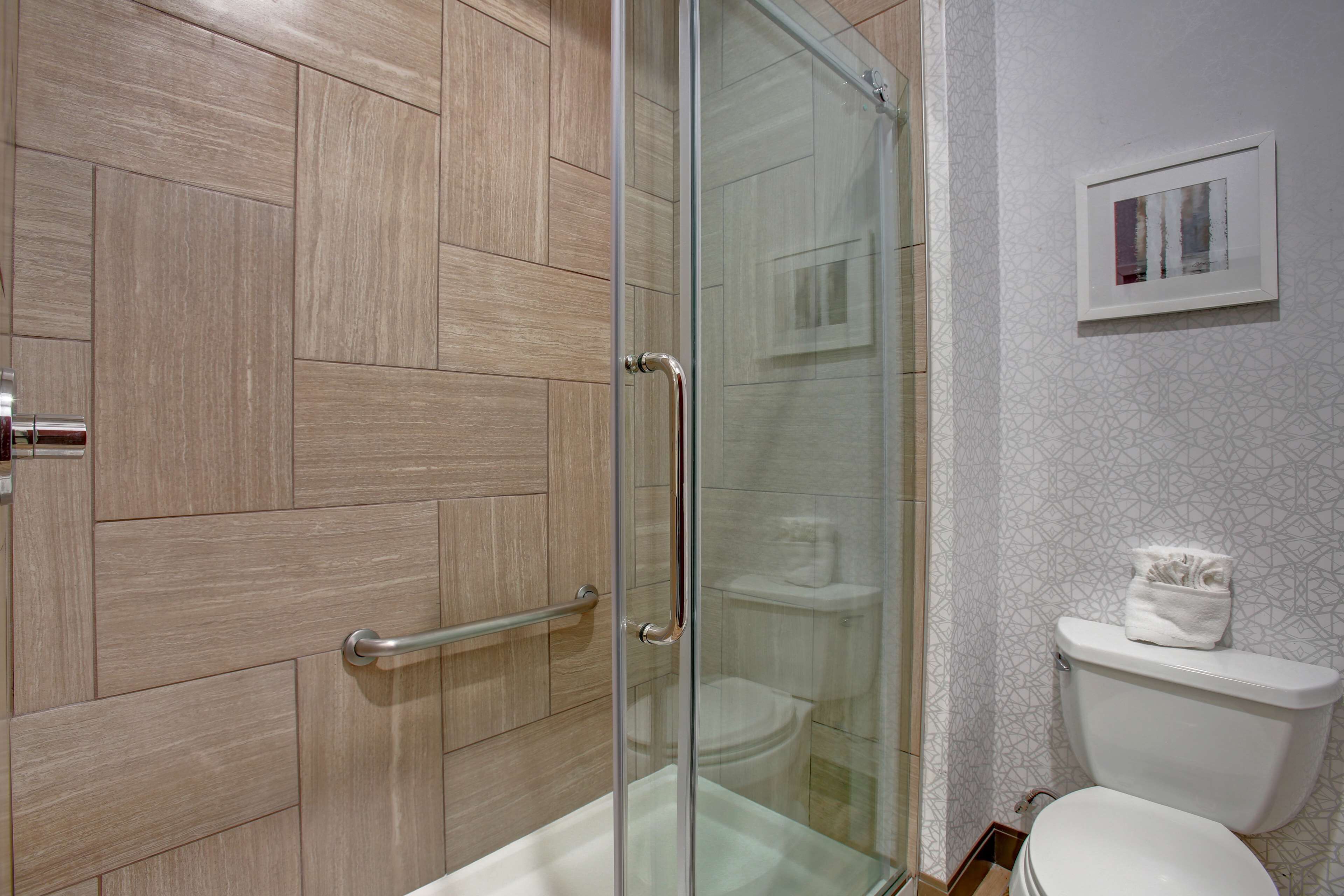 A bathroom with a glass-enclosed shower, wooden paneling, a white toilet, and a framed picture on the wall.