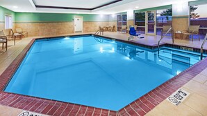 A rectangular indoor swimming pool with clear water, surrounded by lounge chairs and a tiled deck.