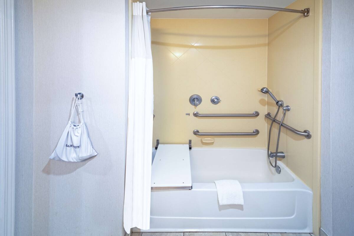 A bathroom with a bathtub, grab bars, a showerhead, and a towel rack.