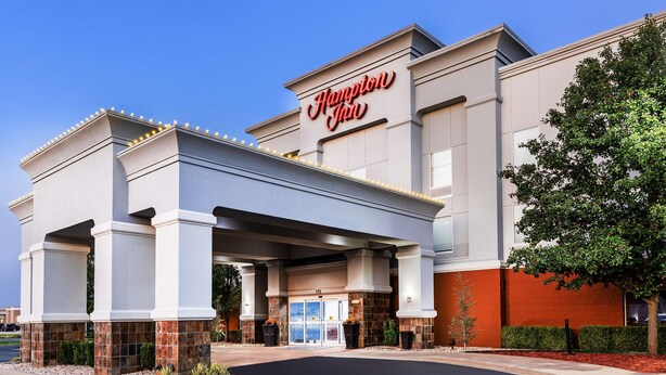A Hampton Inn hotel with a modern facade, large entrance, and a clear sky.