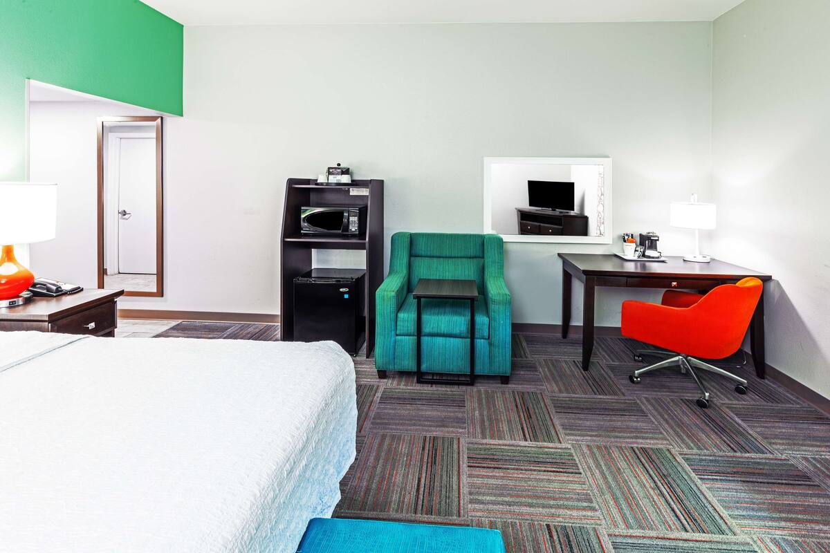 A hotel room with a bed, a desk with a chair, a TV, and a microwave.