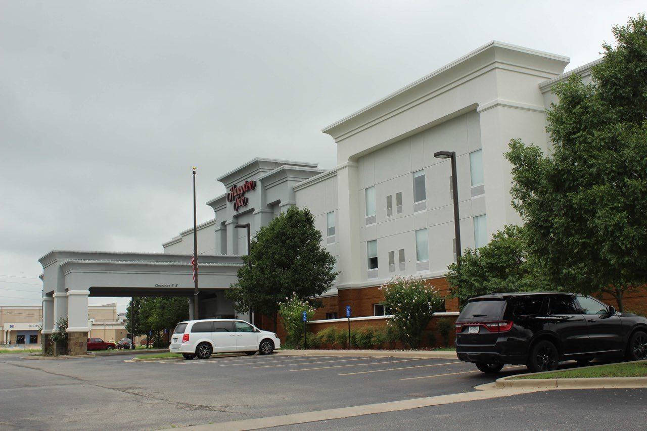 A hotel with a clear entrance, a parking lot, and a large building with a sign.