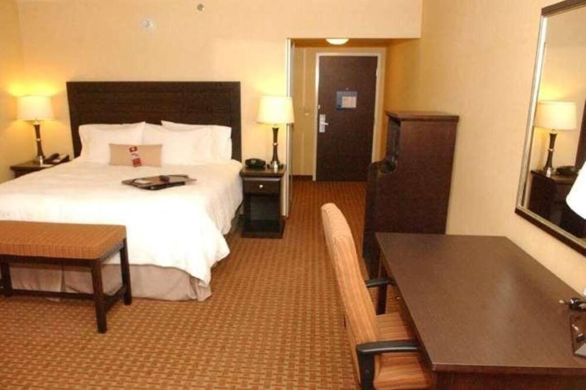 A hotel room with a bed, bedside tables, a desk, a chair, and a mirror.