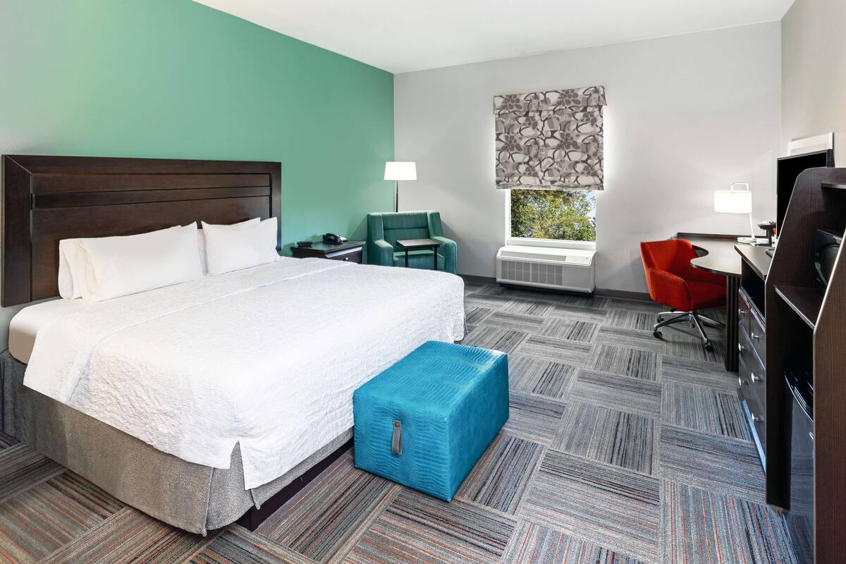 A hotel room with a large bed, a desk, a chair, a TV, and a window with a view.