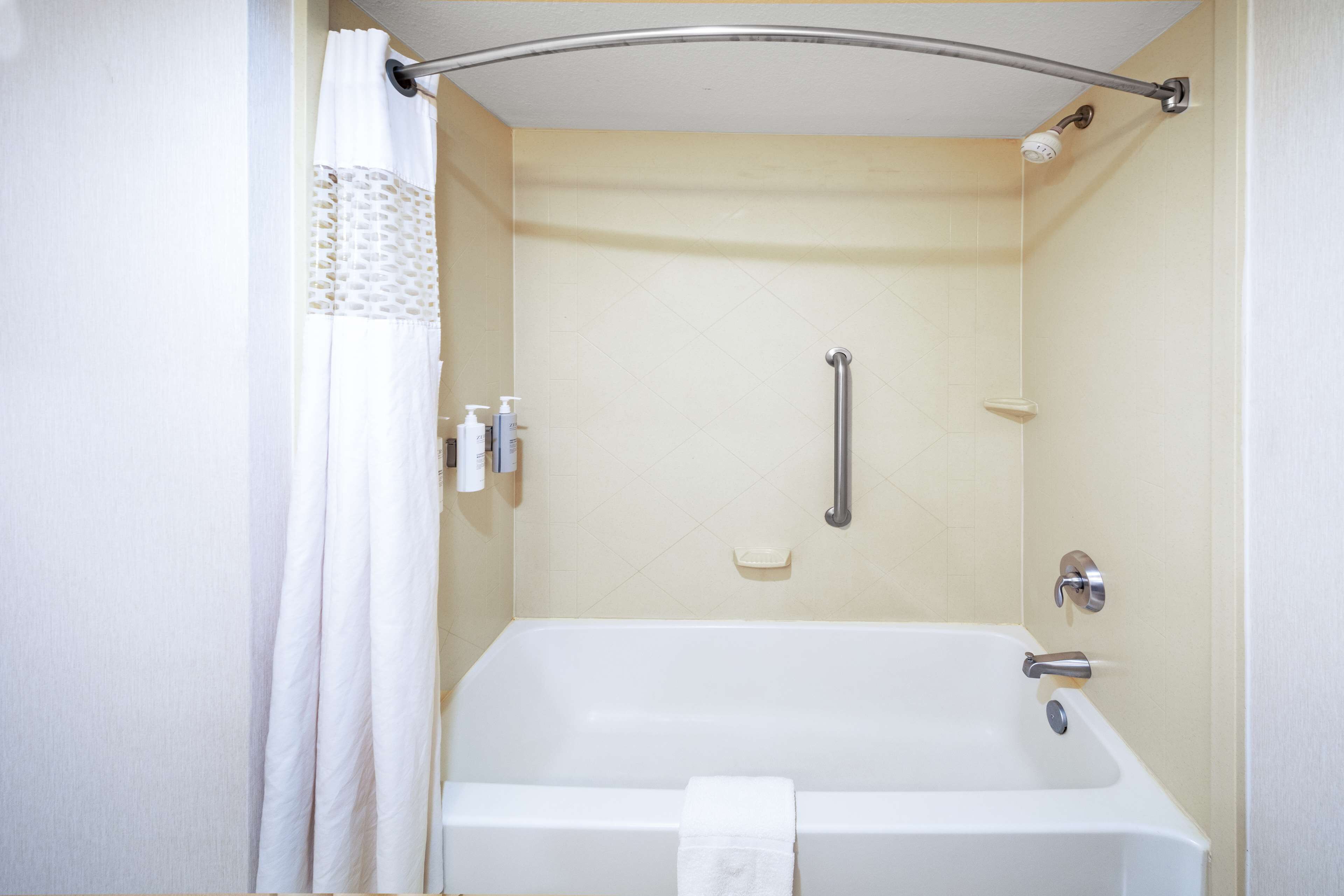 A standard shower stall with a grab bar, a handheld showerhead, and a soap dish.