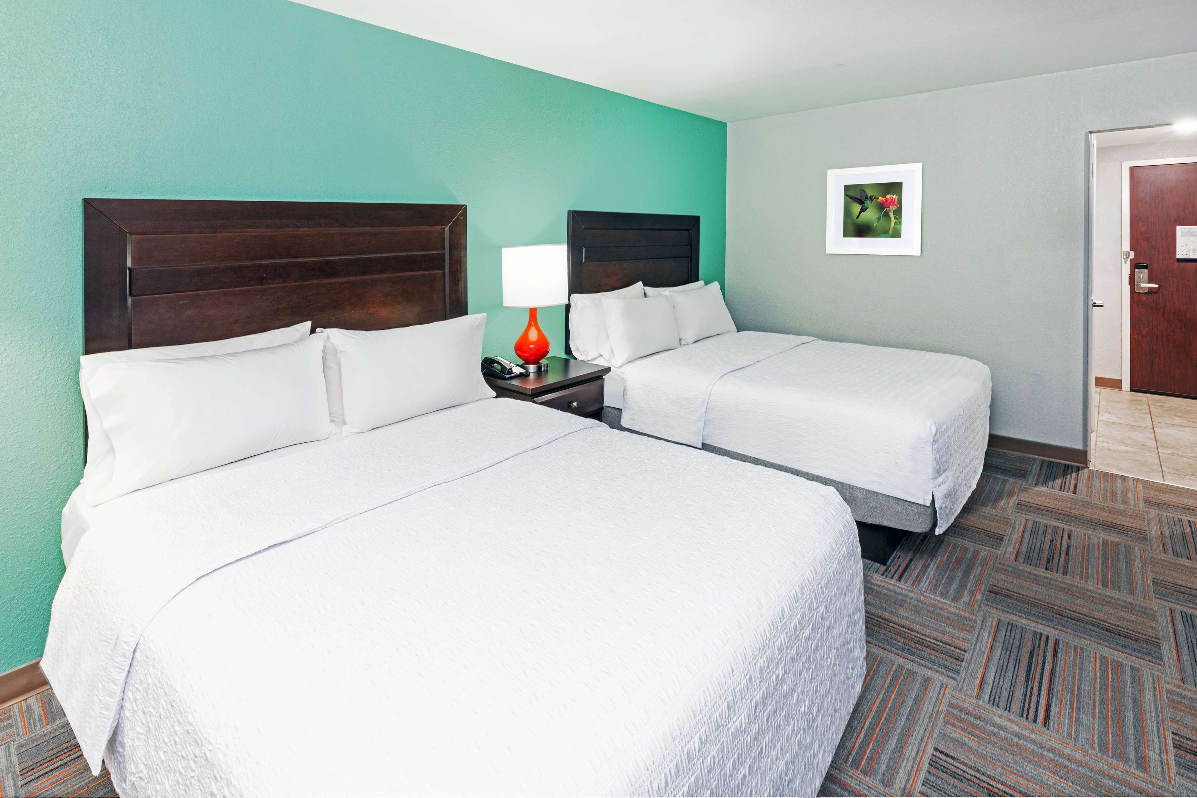 A hotel room with two beds, a nightstand with a lamp, and a door.