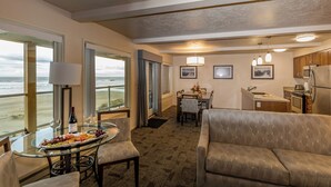 A hotel room with a dining area, kitchen, and large windows overlooking the beach.
