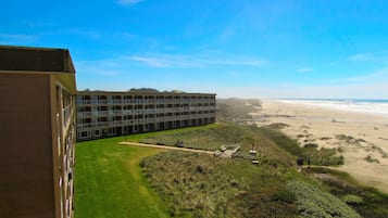 A multi-story building with a flat roof and large windows, overlooking a beach with sand dunes and a clear sky.