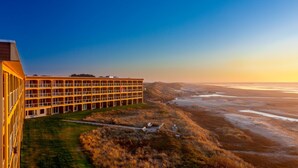 A multi-story hotel with a flat roof and large windows, situated on a grassy hill overlooking a beach and ocean. - Driftwood Shores Resort And Conference Center (Florence)