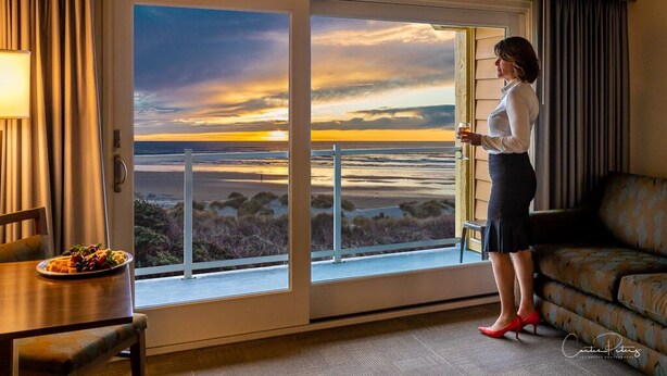 A woman standing by a large sliding glass door with a view of a sunset over a body of water. - Driftwood Shores Resort And Conference Center (Florence)