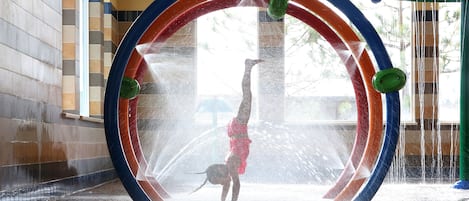 A water play area with a circular water feature and a person performing a handstand.