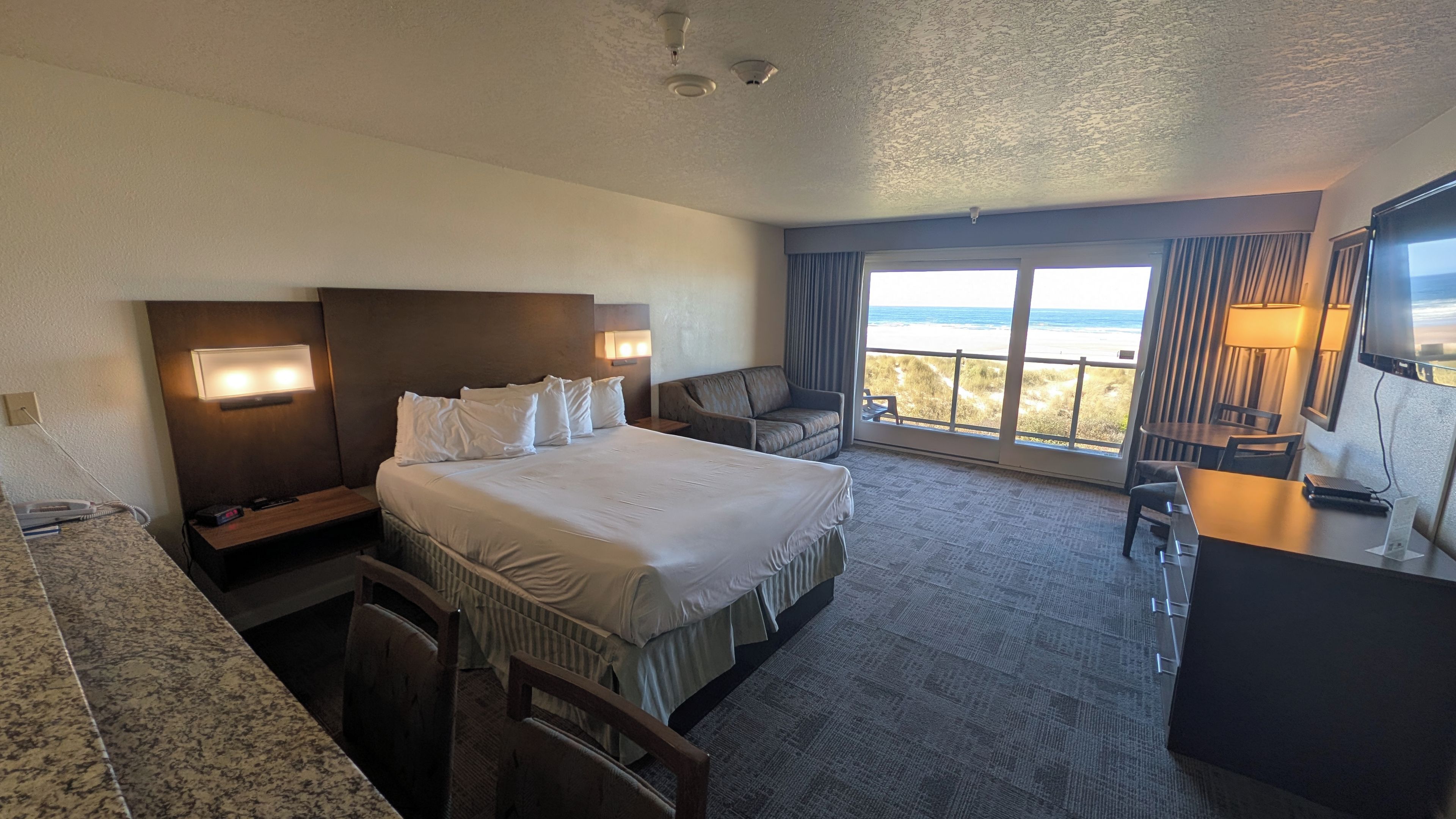 Habitación de hotel con una cama grande, un escritorio, una silla y vistas a la playa.