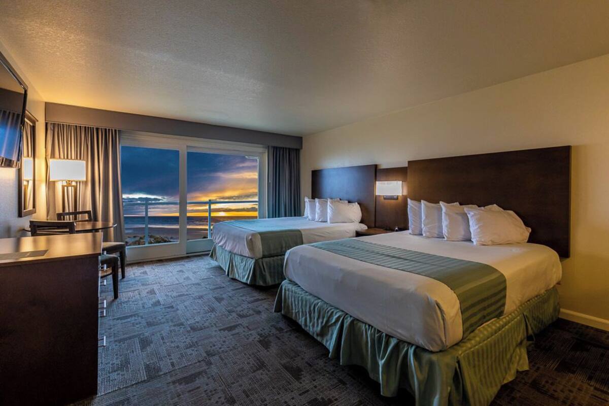 A hotel room with two beds, a desk, and a view of the sunset.