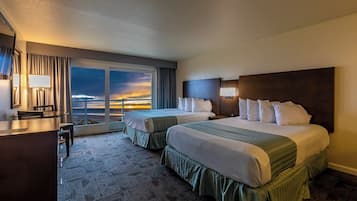 Habitación de hotel con dos camas, un escritorio y vistas al atardecer.