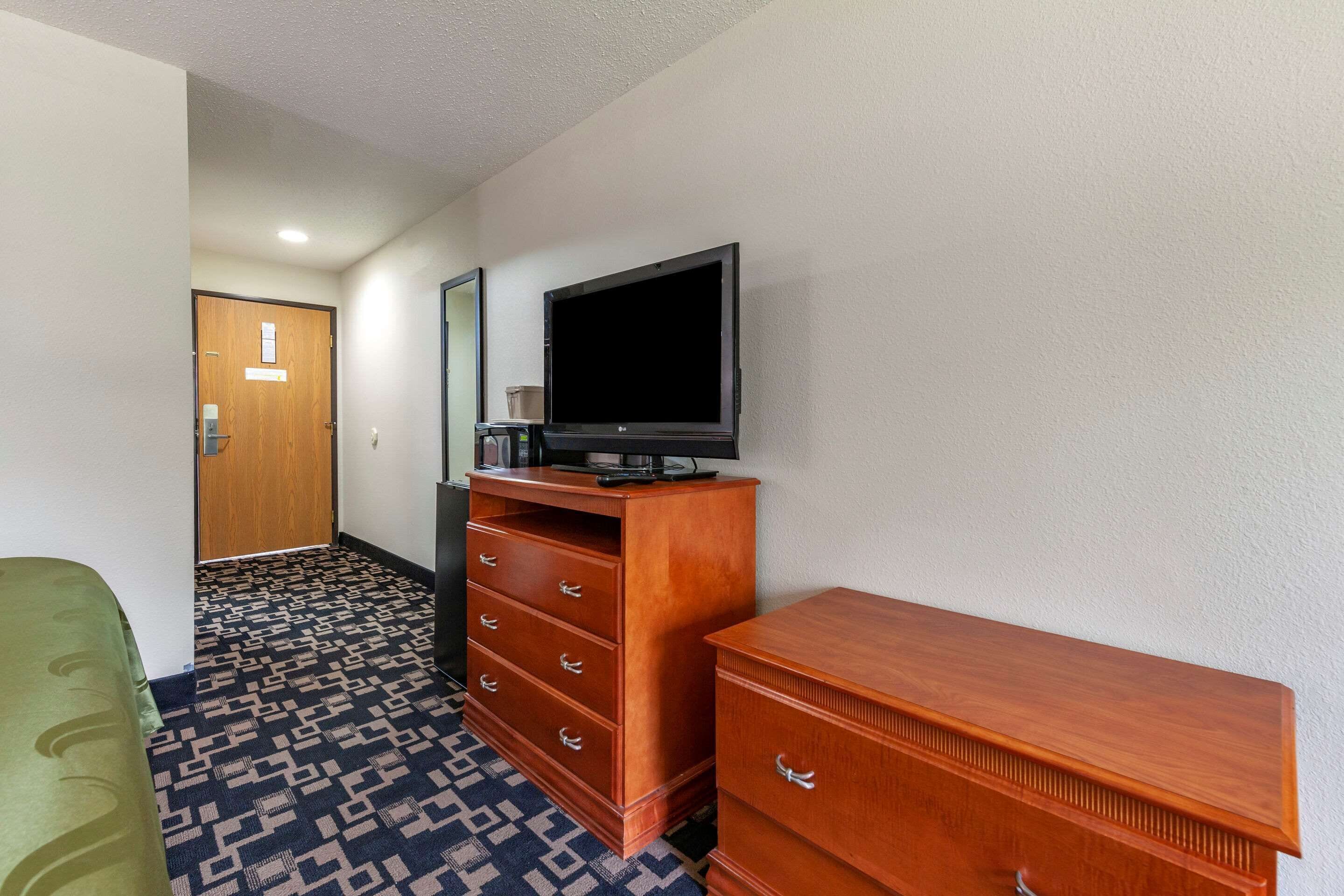 A hotel room with a wooden dresser, a television on top, and a patterned carpet.