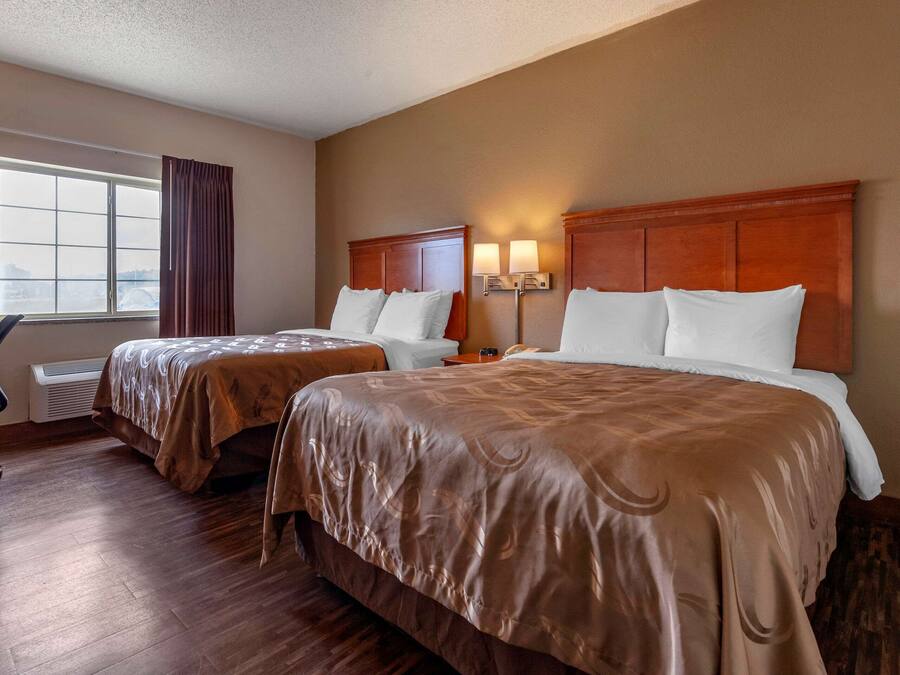 A hotel room with two beds, a desk, and a chair.