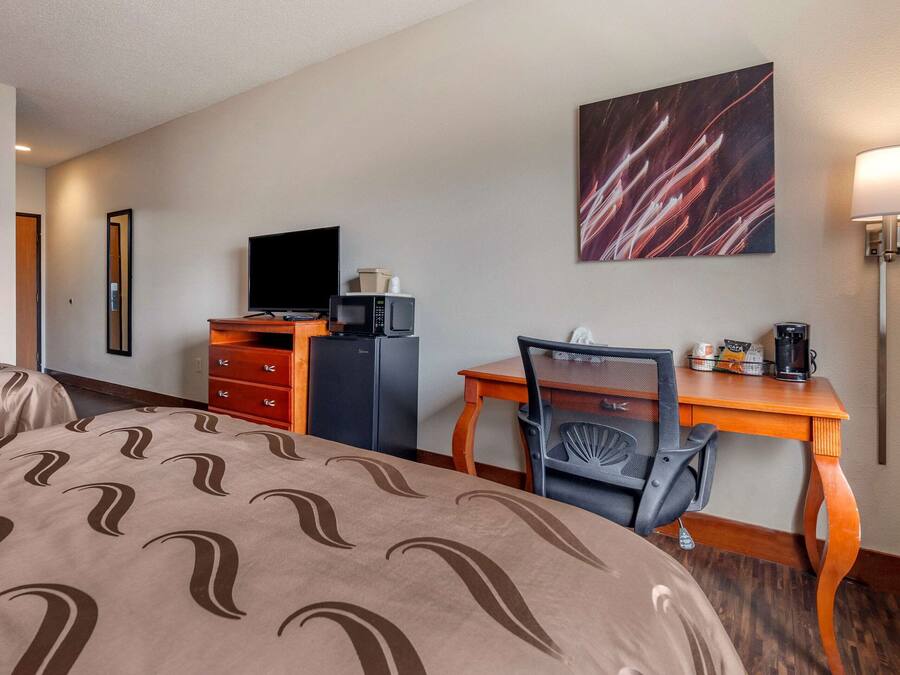 Une chambre d’hôtel équipée d’un lit, d’un bureau, d’une chaise, d’une télévision, d’un four à micro-ondes et d’une machine à café.