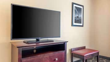 A hotel room with a flat-screen TV on a wooden cabinet, a framed picture on the wall, and a small wooden bench.