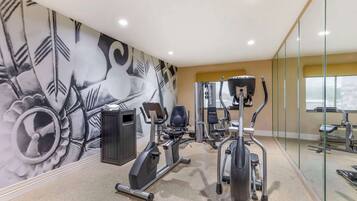 Un gimnasio con equipo de ejercicio, un mural en la pared y un ventanal grande.